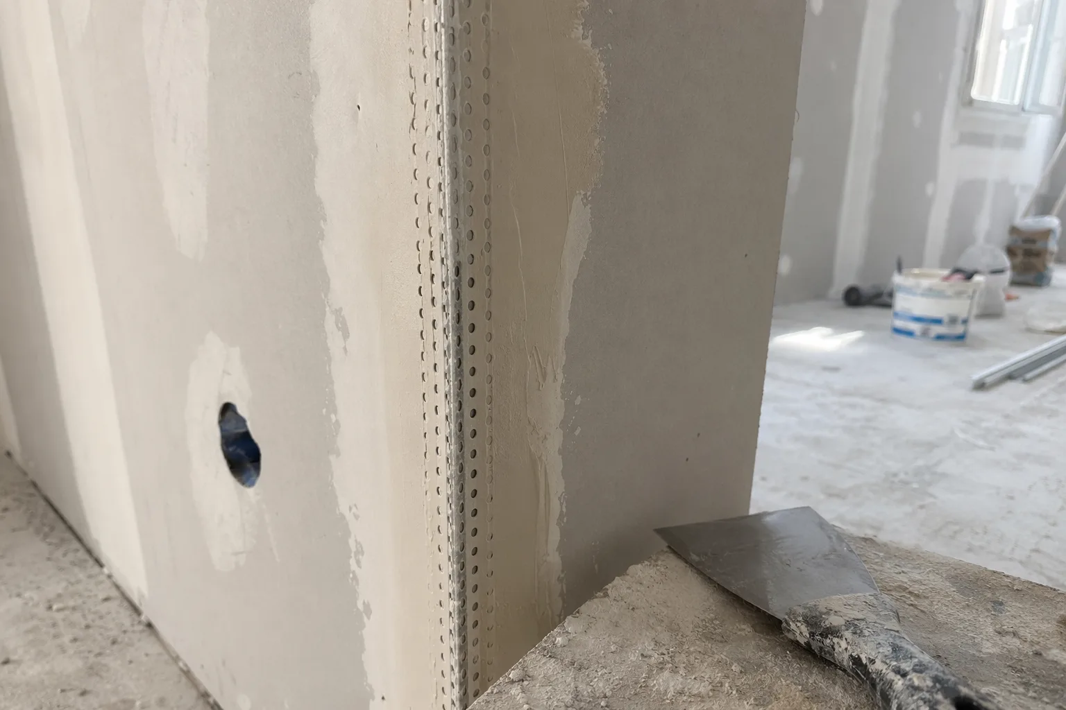 Angolo esterno di una parete in cartongesso in costruzione, con paraspigolo appena allettato nello stucco fresco e spatola appoggiata